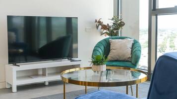 Een moderne woonkamer met een flatscreen televisie, een groene bank, een ronde glazen salontafel en een kamerplant.