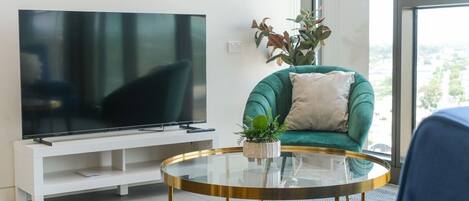 Una sala de estar moderna con un televisor de pantalla plana, un sofá verde, una mesa de centro redonda de vidrio y una planta en maceta.
