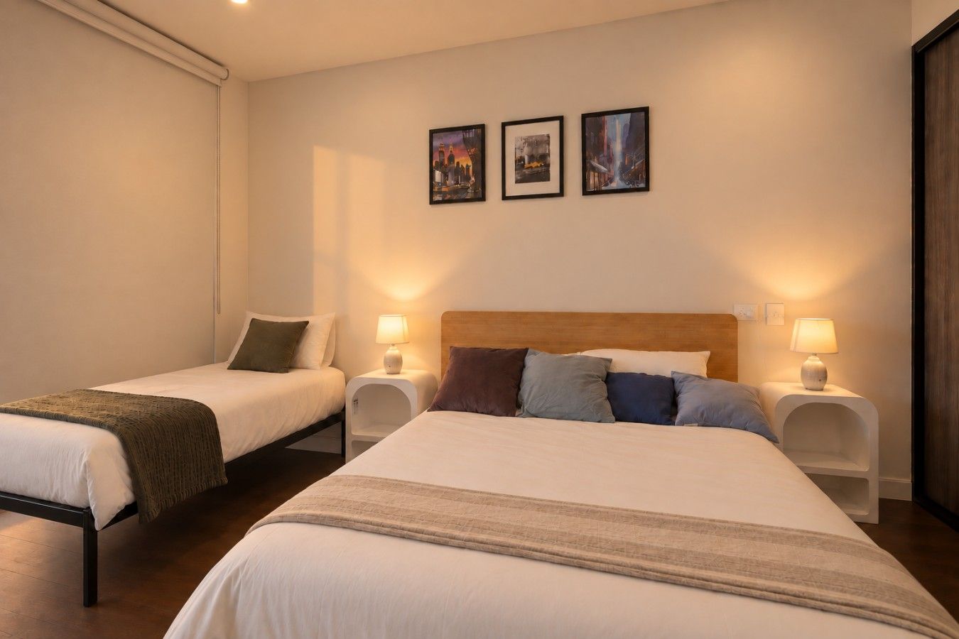 Een hotelkamer met twee bedden, elk met een nachtkastje en lamp. Drie ingekaderde foto's hangen aan de muur.