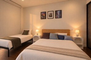 A hotel room with two beds, each with a bedside table and lamp. There are three framed pictures on the wall.