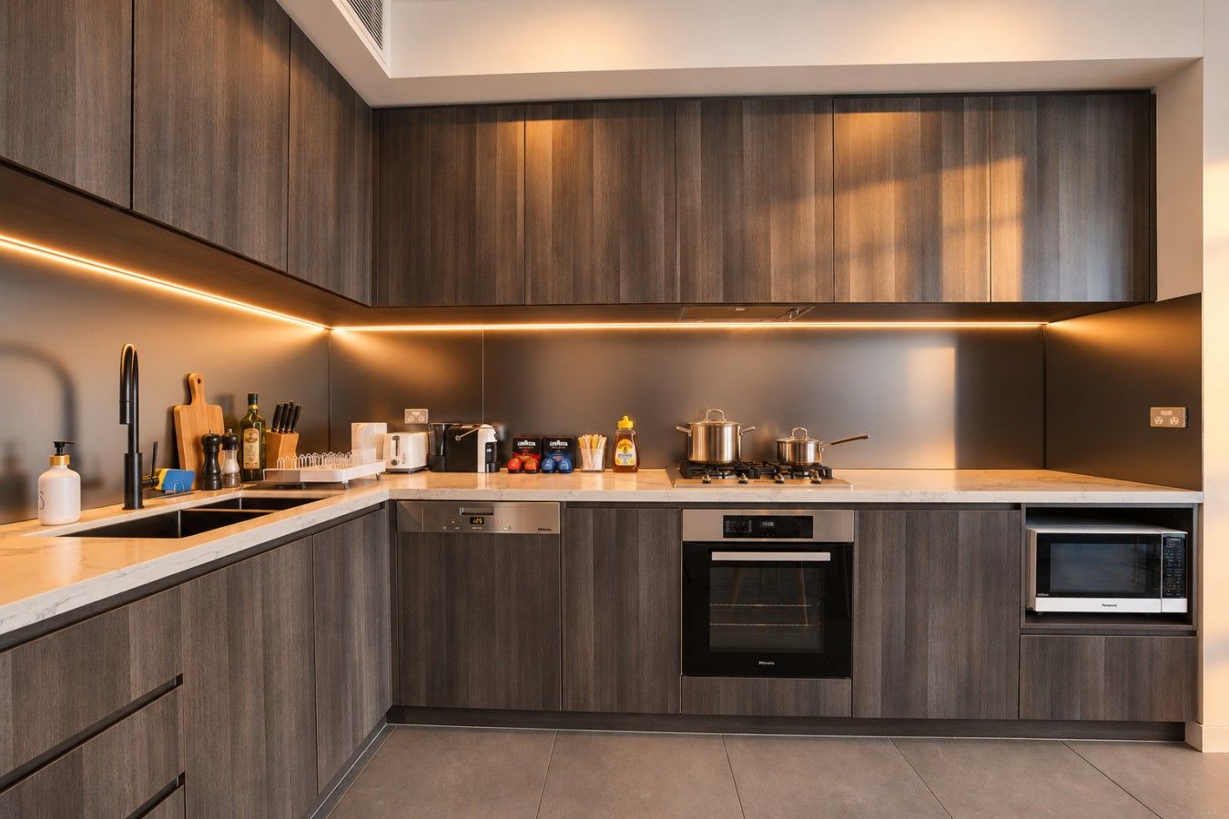 Een moderne keuken met donkere houtkasten, een ingebouwde vaatwasser, een magnetron en een gasfornuis.
