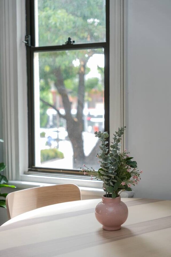 A table with a vase of flowers and a window with a view of trees and buildings.