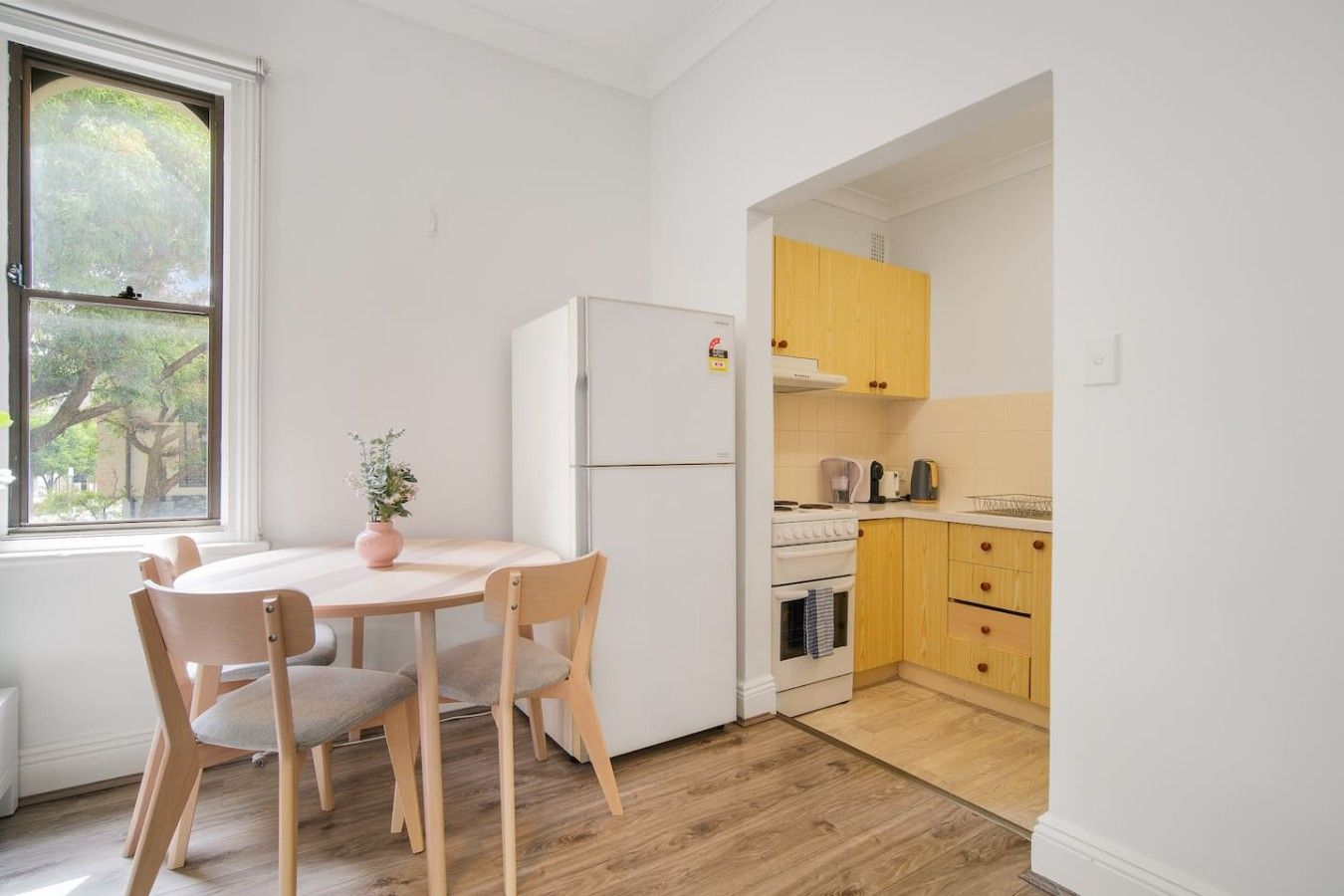 A compact kitchen with wooden cabinets, a white refrigerator, and a dining area with a table and chairs.