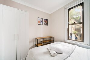 Un dormitorio con cama, armario, ventana con vistas y una pequeña mesa con estante.