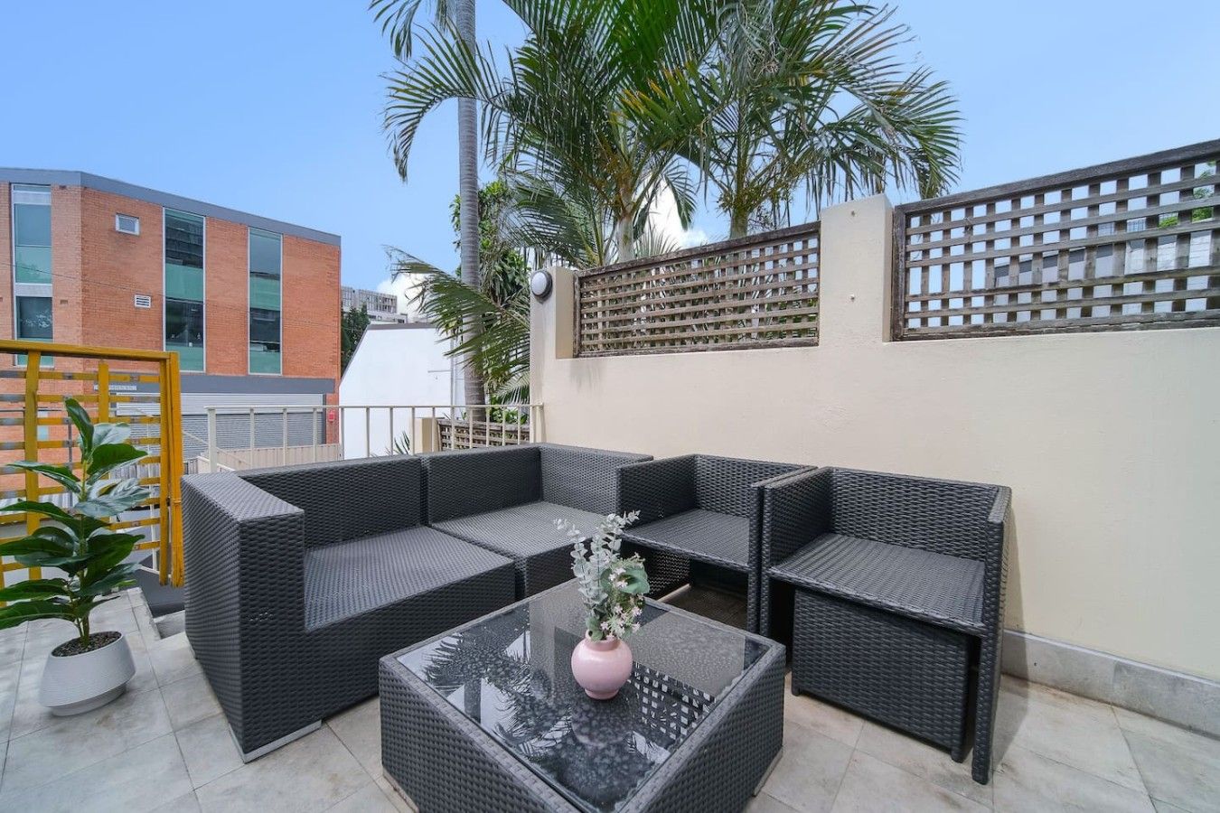 An outdoor patio with wicker furniture, a glass table, and a potted plant.