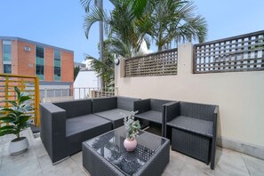 Un patio al aire libre con mobiliario de mimbre, una mesa de vidrio y una planta en maceta.