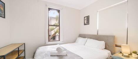 A bedroom with a bed, a desk, a window, and a bedside lamp.