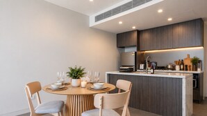Et moderne køkken med en central ø, indbyggede hårde hvidevarer og et spiseområde med et rundt bord og stole.
