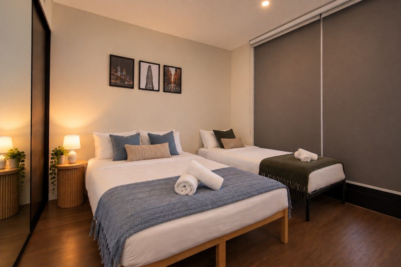 A hotel room with two beds, a large mirror, and a wall with three framed pictures.
