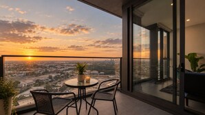 En balkon med et bord, stole, en potteplante og udsigt over bybilledet i solnedgangen.