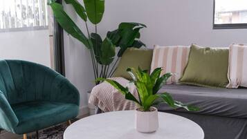 Een moderne woonkamer met een blauwgroene fauteuil, een ronde witte tafel en een grote potplant.