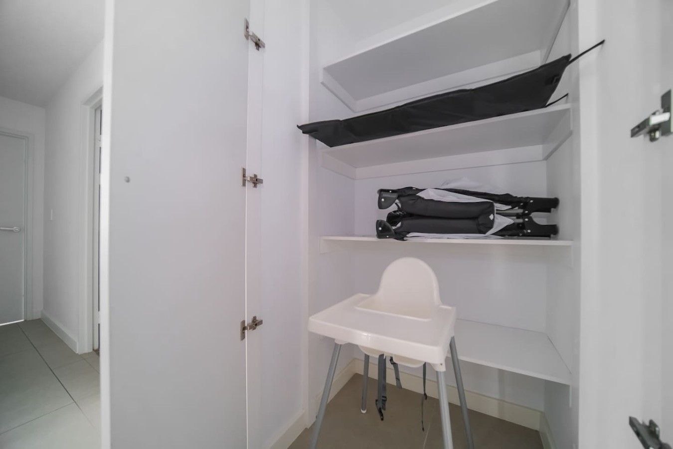 A room with a white door, a white chair, and shelves with folded items.