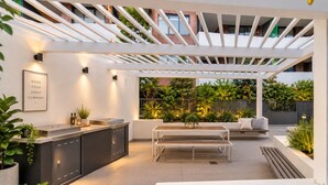 Ett modernt utomhuskök med en inbyggd arbetsbänk, sittplatser och en pergola.