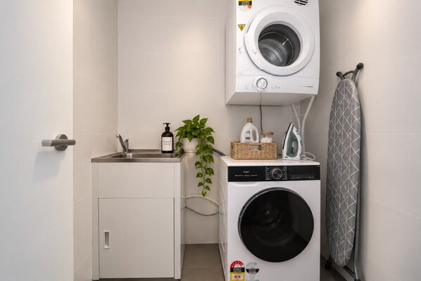 A compact laundry area with a washing machine, a sink, and a drying rack.