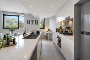 A modern kitchen with a central island, stainless steel appliances, and large windows offering a view of greenery.