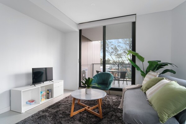 A modern living room with a flat-screen TV, a white console, a round coffee table, a teal chair, and a sofa with striped cushions.