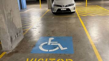 Een parkeergarage met een witte auto geparkeerd in een bezoekersplaats, gemarkeerd met een blauw symbool voor mindervaliden en het woord 'VISITOR' in geel.