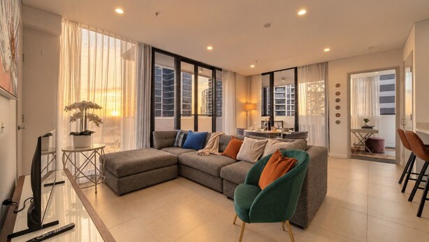 Una sala de estar moderna con un sofá modular, una zona de comedor y vistas de la ciudad a través de amplios ventanales.