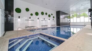 Una piscina interior moderna con agua azul cristalina, rodeada por una solería alicatada y una pared con adornos circulares verdes.