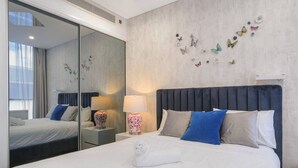 Una habitación de hotel con cama, mesita de noche, lámpara, espejo y decoración de mariposas en la pared.