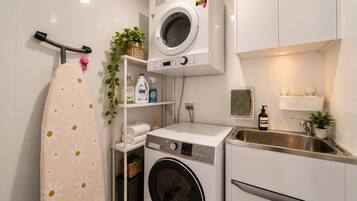 A compact laundry area with a washing machine, dryer, and ironing board.