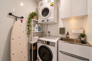 A compact laundry area with a washing machine, dryer, and ironing board.