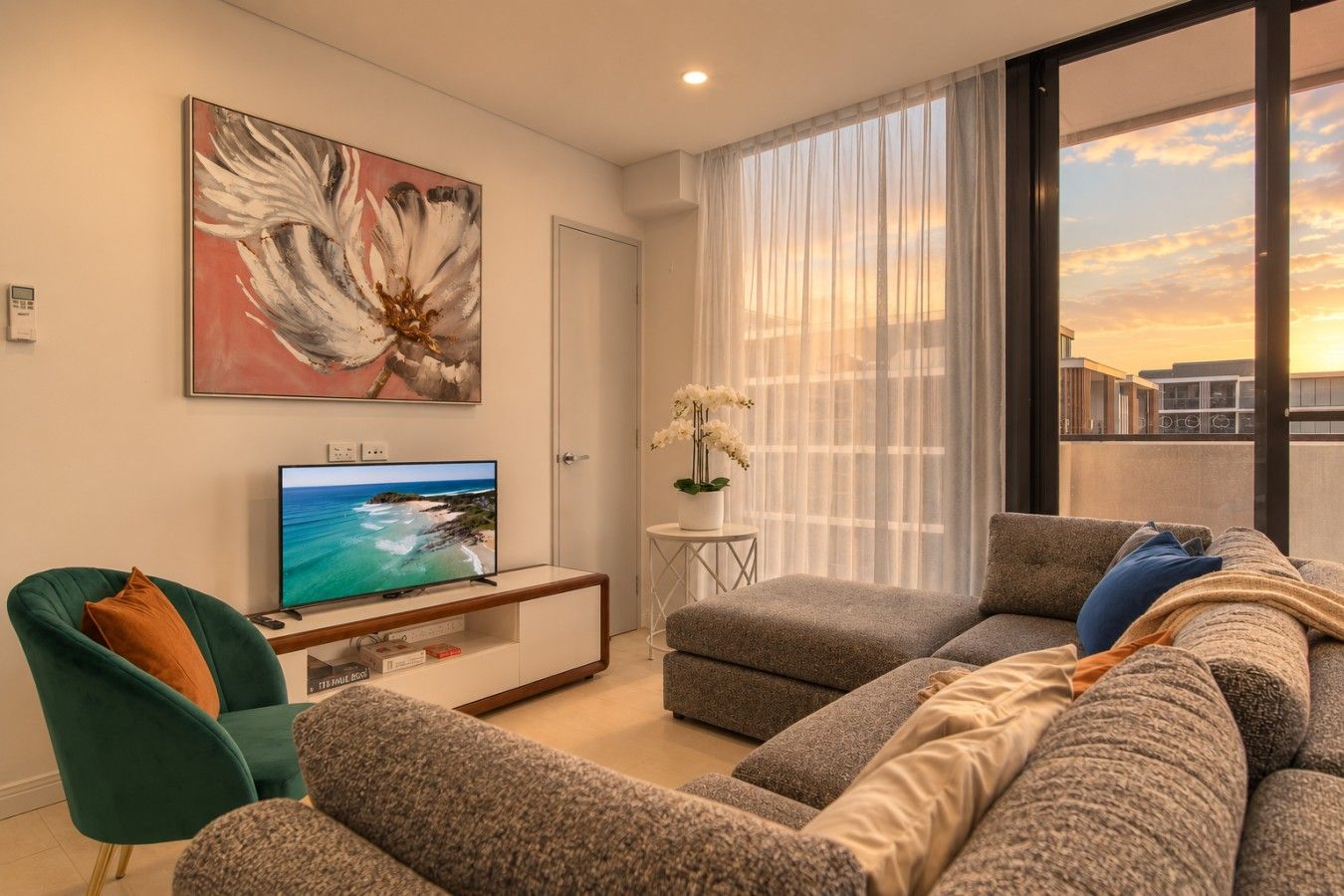 Una sala de estar moderna con un televisor de pantalla plana, un conjunto de sofás, un sillón verde y un amplio ventanal con cortinas.