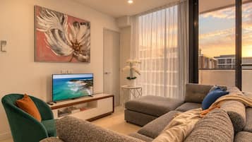 Una sala de estar moderna con un televisor de pantalla plana, un conjunto de sofás, un sillón verde y un amplio ventanal con cortinas.