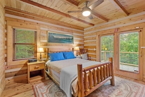 A wooden cabin bedroom with a bed, nightstands, a ceiling fan, and a large window. - 4-bedroom cabin in Seven Devils with stunning mountain views (Seven Devils)