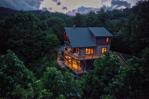 A two-story log cabin with a deck, surrounded by dense forest. - 4-bedroom cabin in Seven Devils with stunning mountain views (Seven Devils)