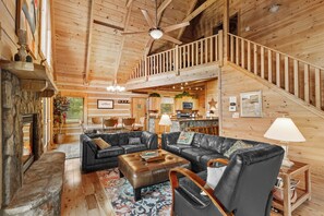 A spacious living area with a fireplace, leather sofas, a dining area, and a wooden staircase. - 4-bedroom cabin in Seven Devils with stunning mountain views (Seven Devils)