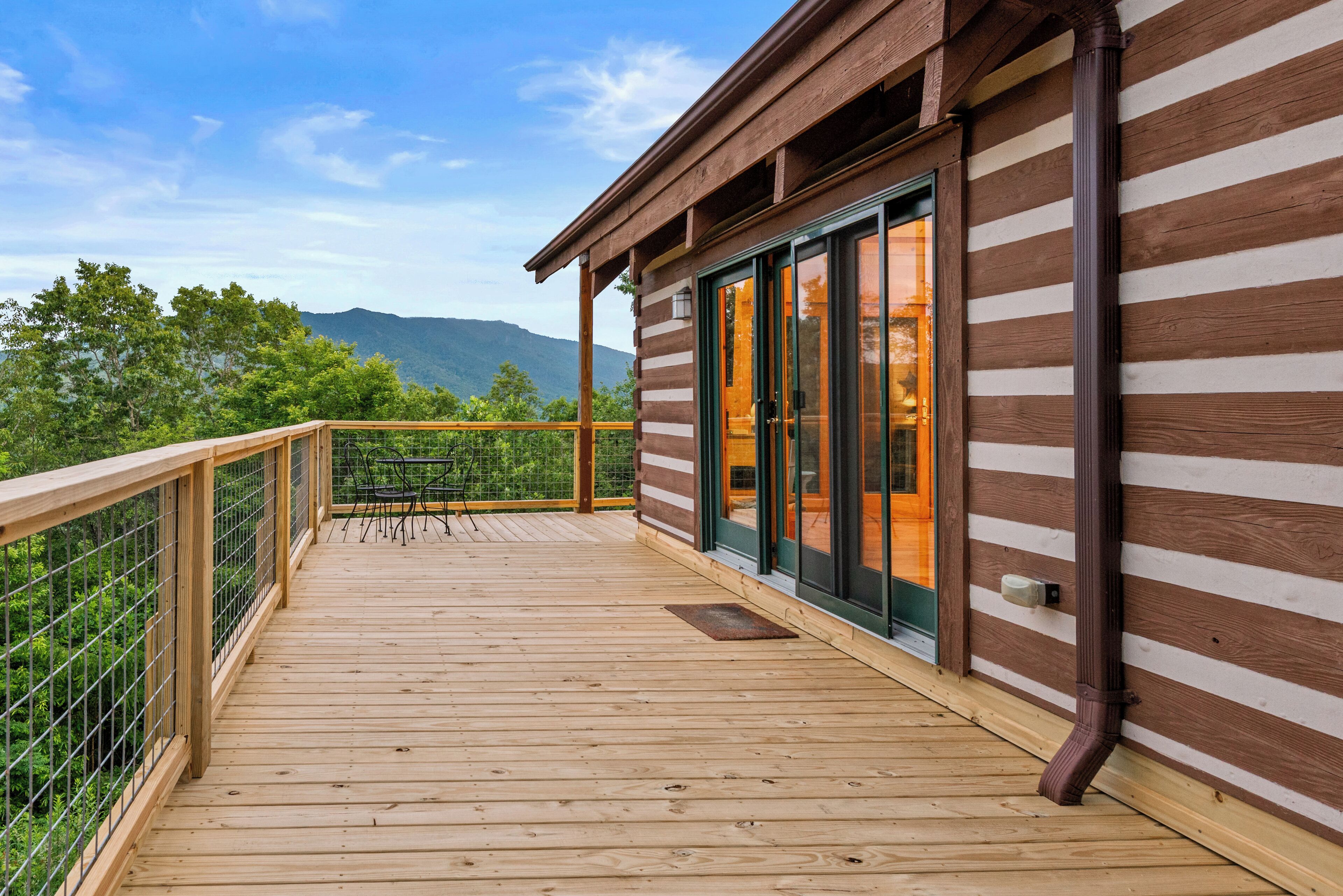 A wooden deck with a railing, a sliding glass door, and a view of mountains.