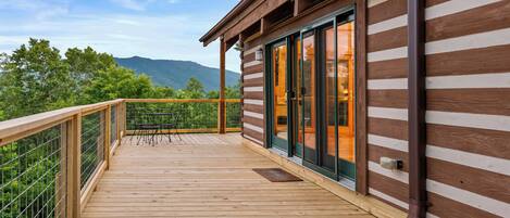 A wooden deck with a railing, a sliding glass door, and a view of mountains.