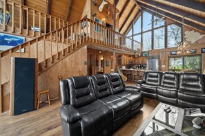 Ein großzügiger Wohnbereich mit einer Holztreppe, Ledersofas und einem großen Fenster mit Blick ins Freie.