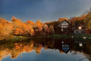 Ein Seehäuschen mit Spiegelbild, umgeben von Herbstlaub.