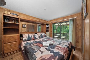 A bedroom with a large bed, built-in wooden shelving, and a sliding glass door to a deck. - Lakefront luxury awaits at Beech Mountain Ski and Lake Chalet! (Beech Mountain)