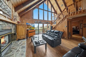 Ein geräumiges Wohnzimmer mit Kamin aus Stein, einer Ledersofa und einer Holztreppe.
