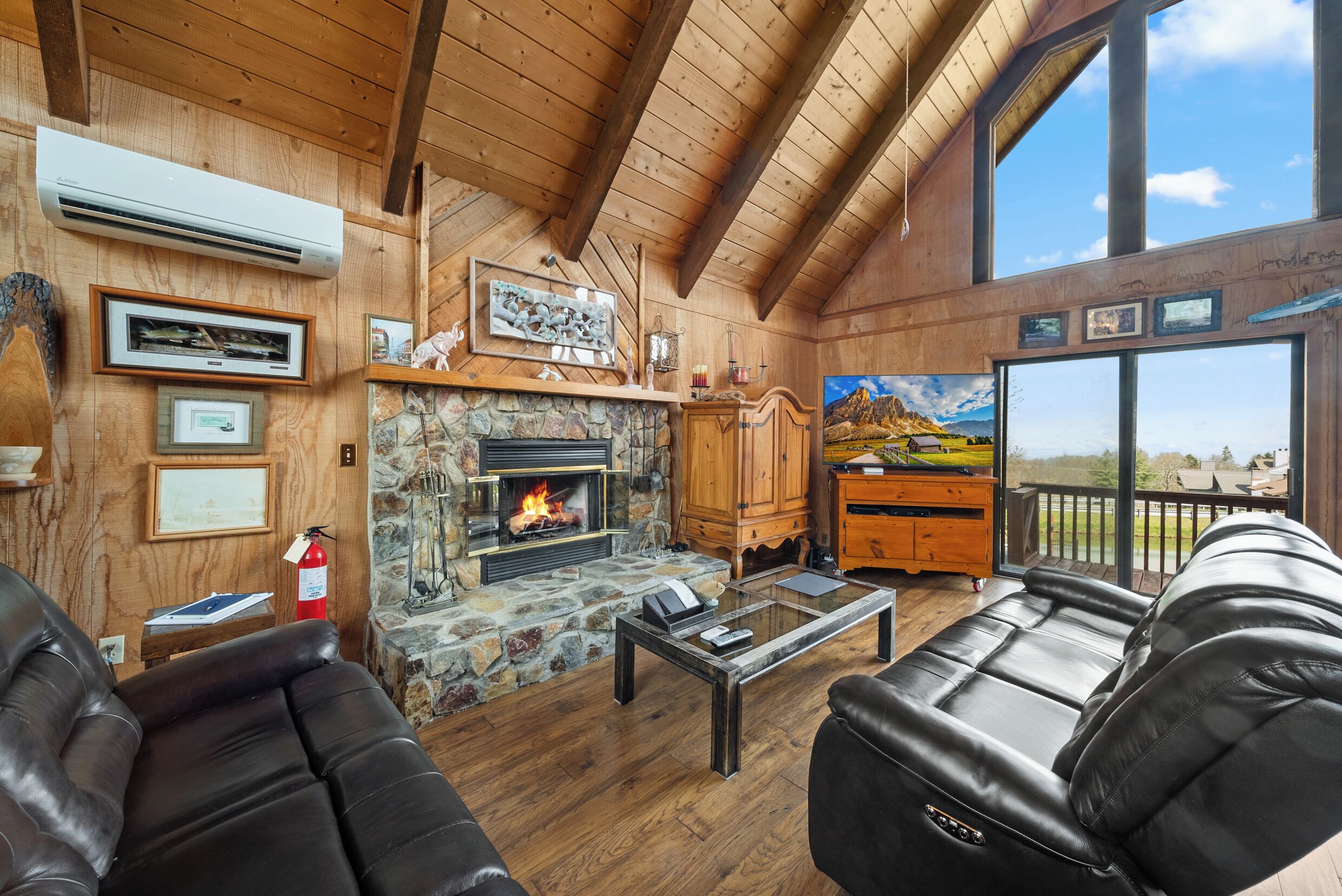 A cozy lodge with a stone fireplace, leather sofas, and a large window offering a scenic view.