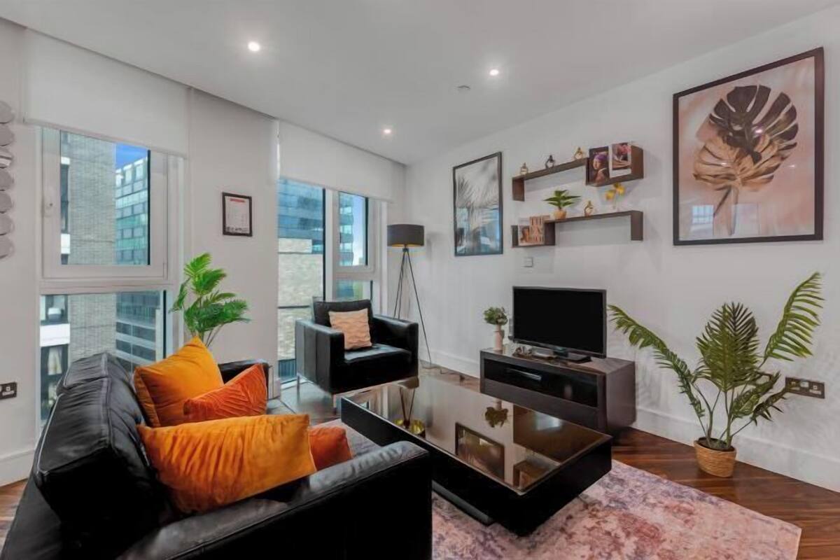 A modern living room with a black sofa, a glass coffee table, a flat-screen TV, and a large window.