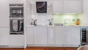 Une cuisine moderne avec des meubles blancs, un four encastré, un micro-ondes, un évier et un égouttoir à vaisselle.