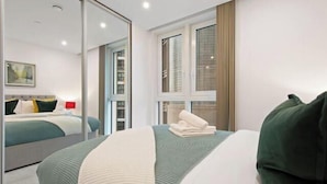 Une chambre d’hôtel avec un lit, un grand miroir, une fenêtre avec des rideaux et une vue sur les bâtiments environnants.