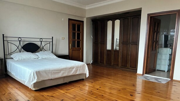 A bedroom with a wooden floor, a bed with white bedding, and a wardrobe with mirrored doors. - Room-goat House Near the Airport (Arnavutköy)
