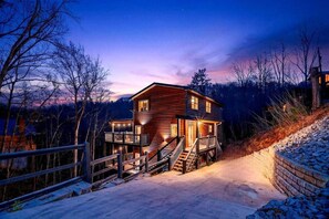 A two-story log cabin with a deck and stairs, surrounded by trees and a snowy landscape. - Family Cabin Retreat | Hot Tub, Decks & Fire Pit (Gatlinburg)