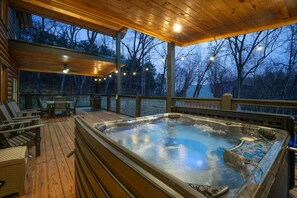 Ein Whirlpool auf einer Holzterrasse mit Stühlen und einem Tisch, umgeben von Bäumen.