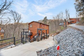 A wooden cabin with a staircase, a concrete pathway, and a stop sign. - Family Cabin Retreat | Hot Tub, Decks & Fire Pit (Gatlinburg)