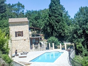 Un edificio de piedra con piscina, rodeado de árboles.