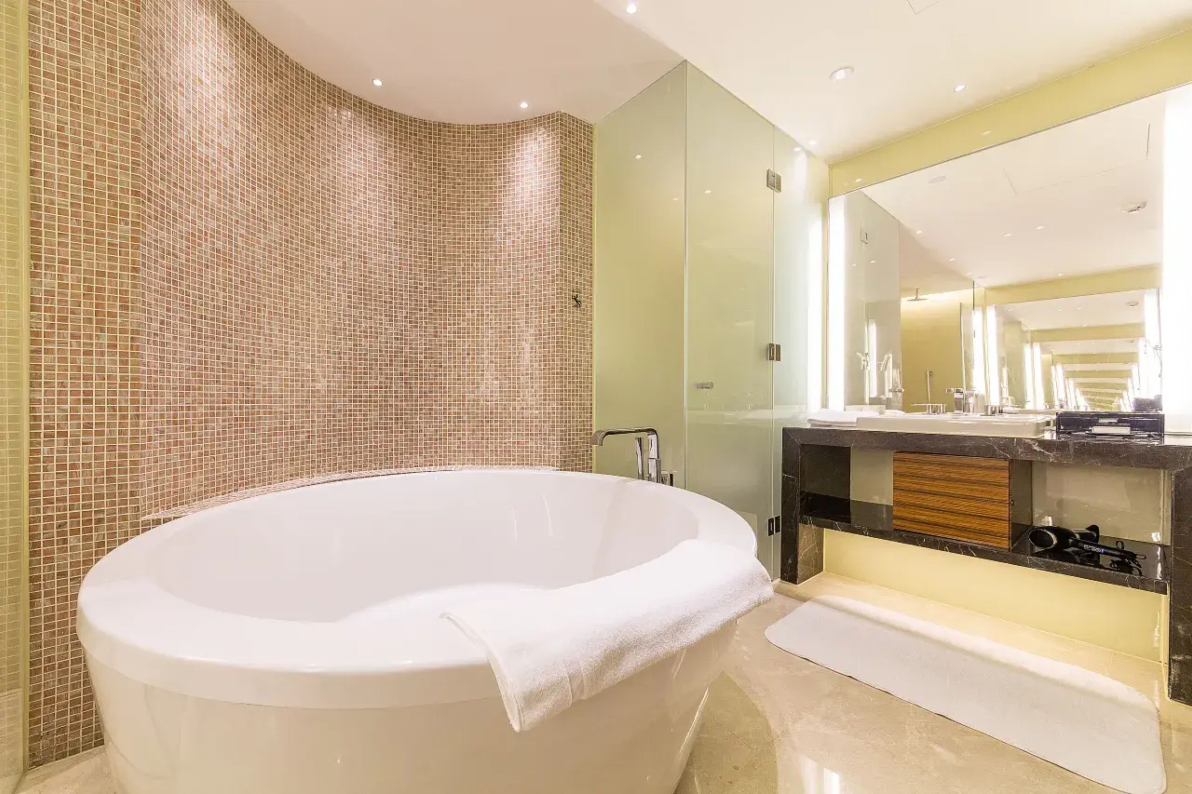 Un baño moderno con una bañera independiente, un espejo grande y un mueble de tocador con panel de madera.