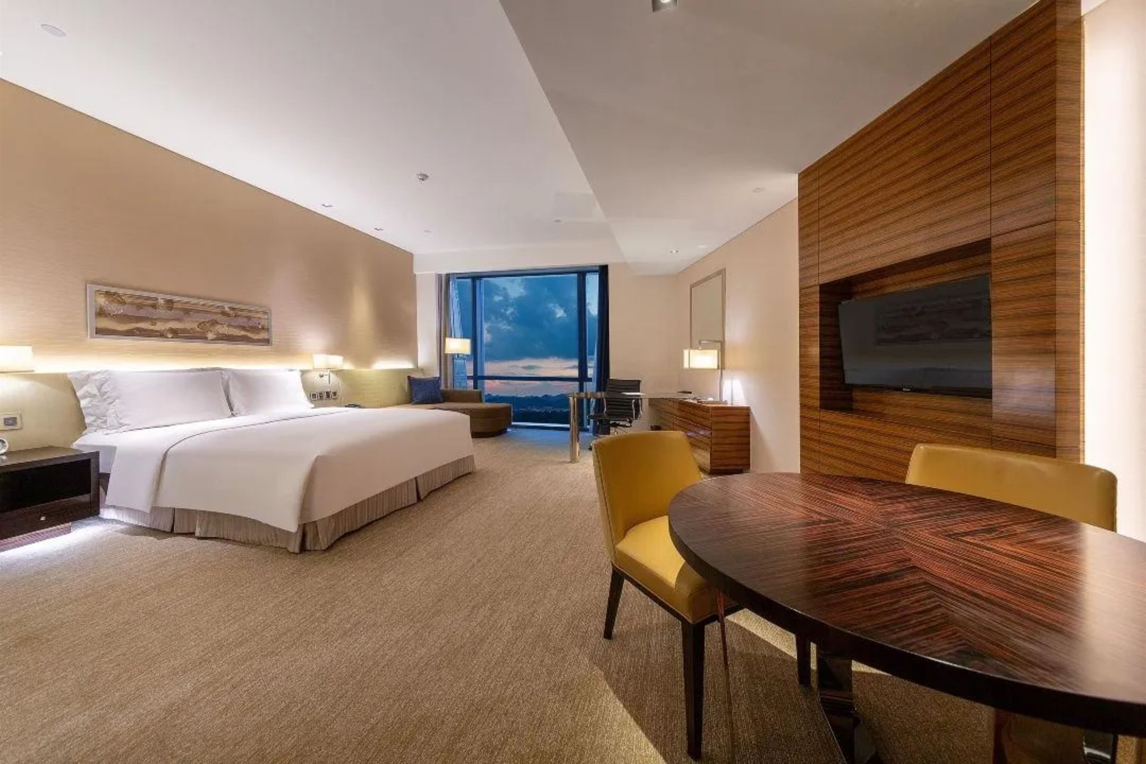 Una habitación de hotel con cama, mesa de comedor, televisor y un ventanal grande.