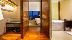 A hotel room with a wooden floor, a bed, a bathtub, and a view of the city at night. - Guiyanghengshiji Hotels (Guiyang)