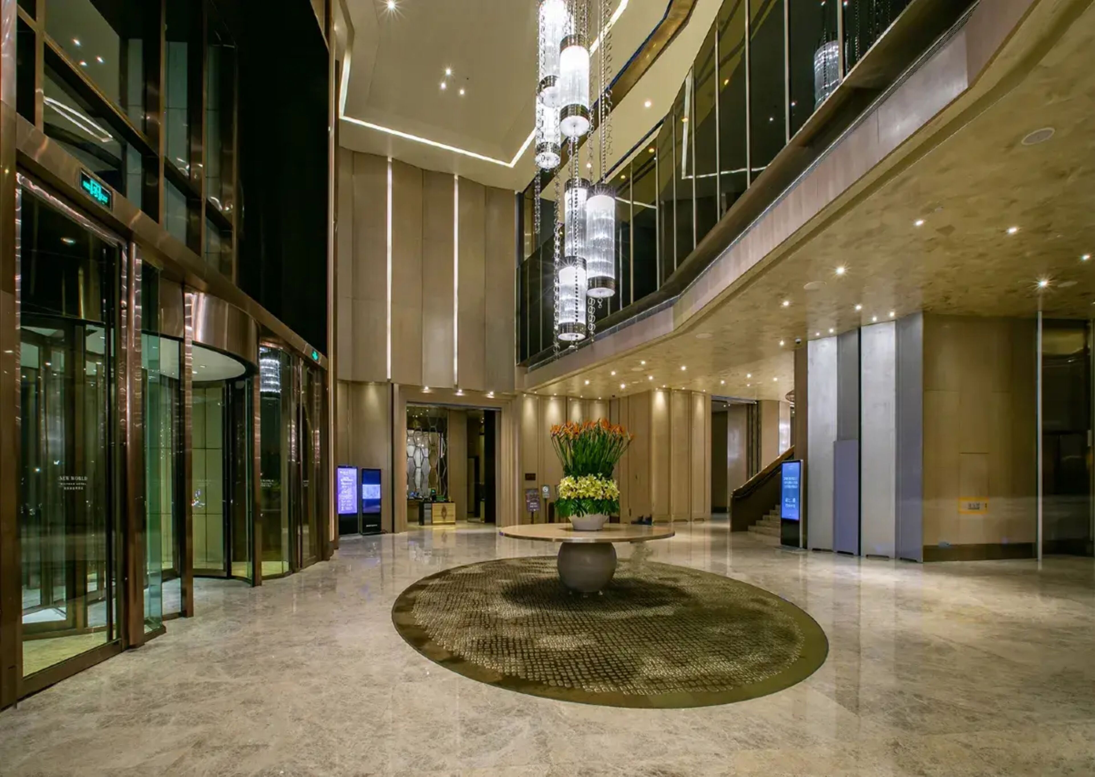 A spacious lobby with a central fountain, glass doors, and a modern chandelier.